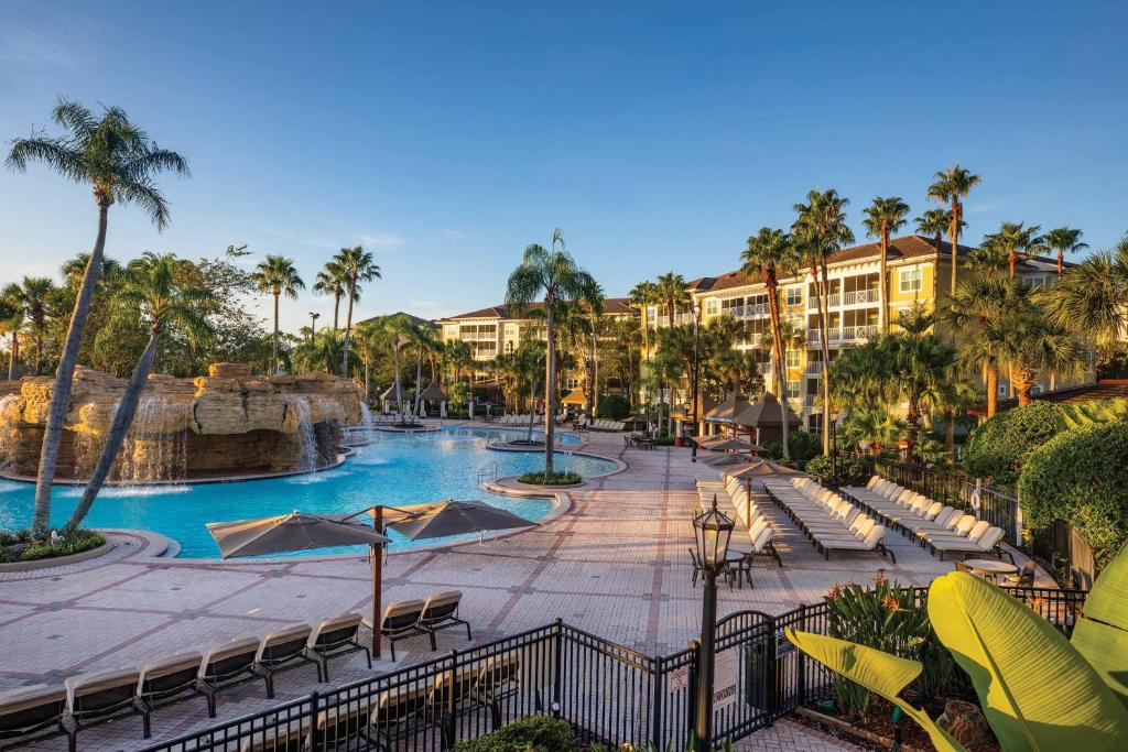 fachada com vista da área externa com cadeiras de praia, algumas palmeiras distribuídas por lá, com piscina com cascata no Sheraton Vistana Villages Resort Villas, um dos resorts em Orlando
