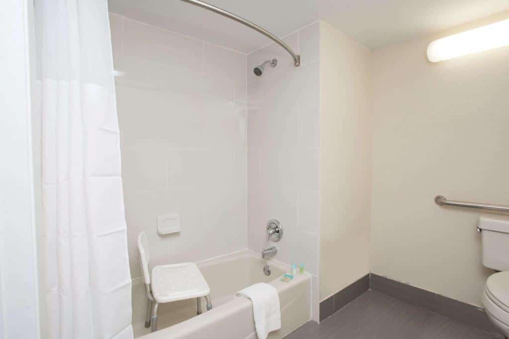 banheiro com adaptações no Days Inn & Suites by Wyndham Orlando Airport, com banheira e box de cortina, cadeira de banho e barras de apoio no vaso
