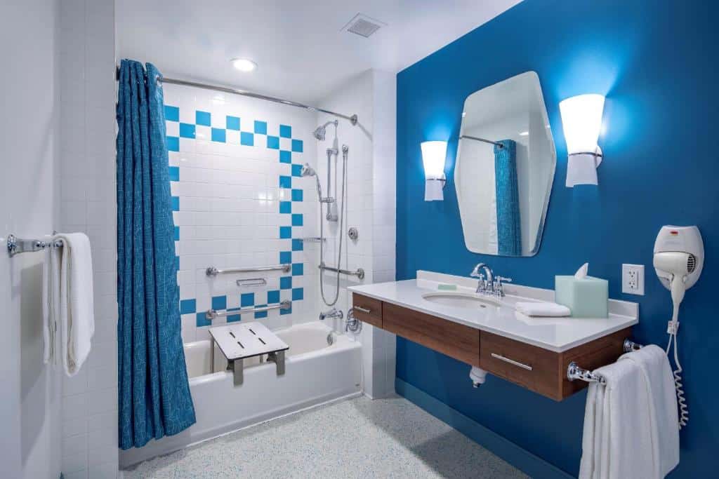 banheiro com adaptações para pcds, com pia mais baixa com espaço para cadeira de rodas, chuveirinho, cadeira de banho e barras de apoio no box de cortinas no Universal's Cabana Bay Beach Resort, um dos hotéis da Universal em Orlando