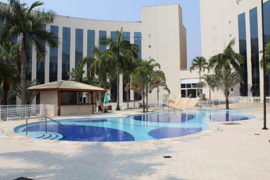 Parte de fora do hotel que mostra a piscina ao ar livre, um quiosque e algumas palmeiras durante o dia.