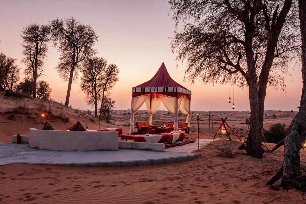 Um bangalô no Bedouin Oasis Desert Camp- Ras Al Khaimah em meio ao deserto com algumas árvores e outros sofás com almofadas