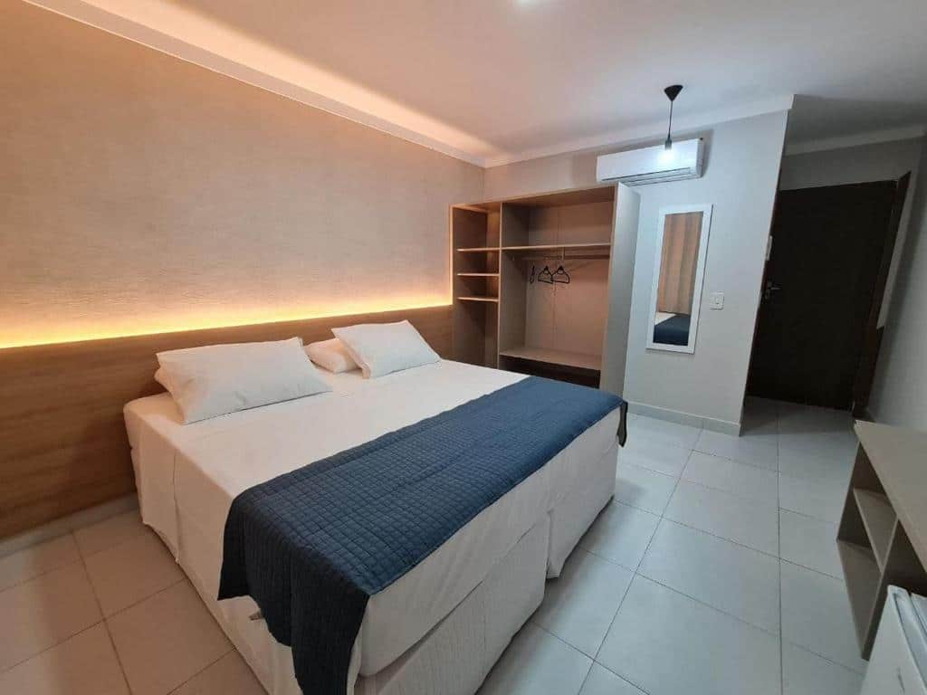 Quarto de hotel com cama de casal, armário de madeira, ar-condicionado e luz de led em cima de cabeceira de madeira. Imagem para ilustrar o post hotéis em Parnaíba.
