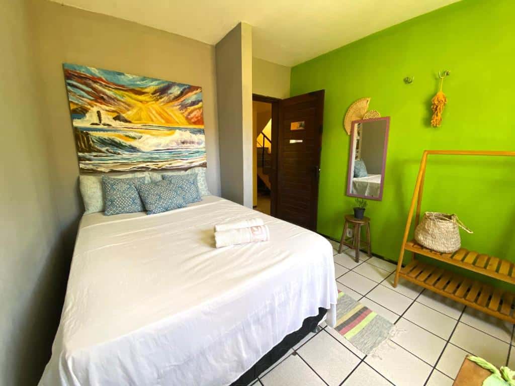 Quarto de hostel com cama de casal, quadro decorativo, parede verde, pequeno armário em madeira e espelho. Imagem para ilustrar o post hotéis em Parnaíba.