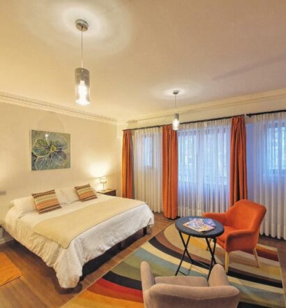 Quarto do Hostal Boutique Casa La Barca com cama de casal no centro do quarto e em frente a cama duas poltronas com mesa de centro. Representa hostels em Santiago.