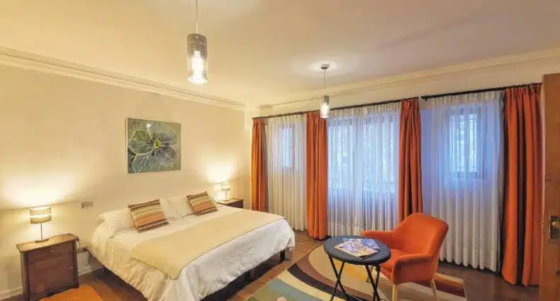 Quarto do Hostal Boutique Casa La Barca com cama de casal no centro do quarto e em frente a cama duas poltronas com mesa de centro. Representa hostels em Santiago.