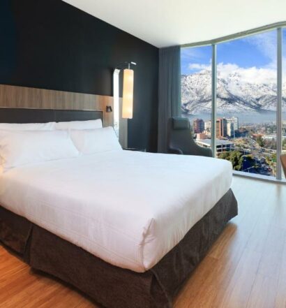 Quarto do Icon Hotel, em Santiago, com cama de casal no centro do quarto do lado esquerdo do quarto janelas panorâmicas com vista das montanhas. Representa Hotéis com vista para as Cordilheiras dos Andes em Santiago.