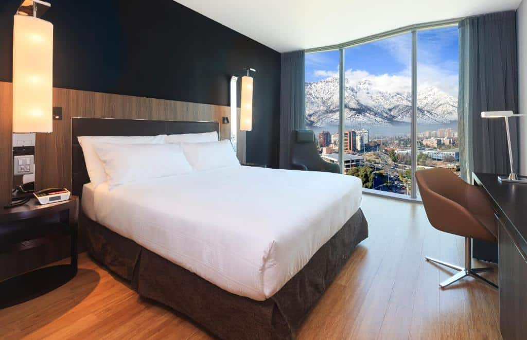 Quarto do Icon Hotel, em Santiago, com cama de casal no centro do quarto do lado esquerdo do quarto janelas panorâmicas com vista das montanhas. Representa Hotéis com vista para as Cordilheiras dos Andes em Santiago.