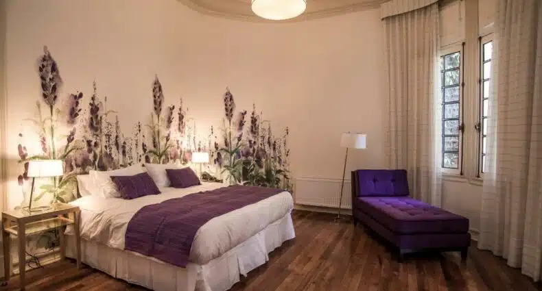 Quarto do Matildas Hotel Boutique com cama de casal do lado esquerdo e do lado esquerdo do quarto uma poltrona roxa. Representa hotéis em boutique em Santiago.