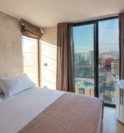Quarto do Zip Housing El Golf com cama de casal do lado esquerdo e ao fundo uma vidraça que tem vista para a cidade. Representa Airbnb em Santiago.