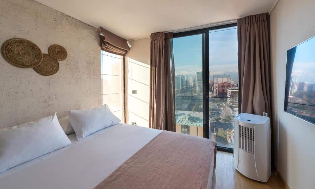 Quarto do Zip Housing El Golf com cama de casal do lado esquerdo e ao fundo uma vidraça que tem vista para a cidade. Representa Airbnb em Santiago.