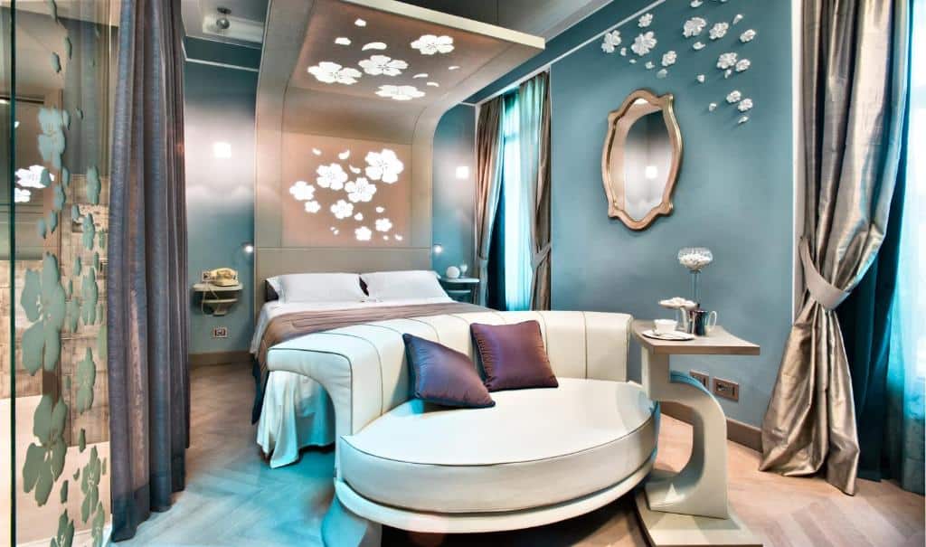Quarto do Château Monfort – Relais & Châteaux com uma cama de casal, um pequeno espelho, um sofá arredondao com almofadas, uma mesinha de centro e duas janelas, para representar onde ficar em Milão