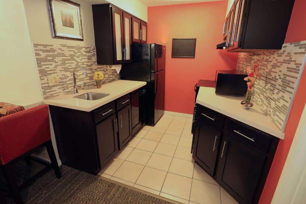 cozinha do Sonesta ES Suites Orlando - Lake Buena Vista, um dos hotéis com cozinha em Orlando, que conta com pia, forno e fogão, micro-ondas, geladeira e armários em preto com louças brancas