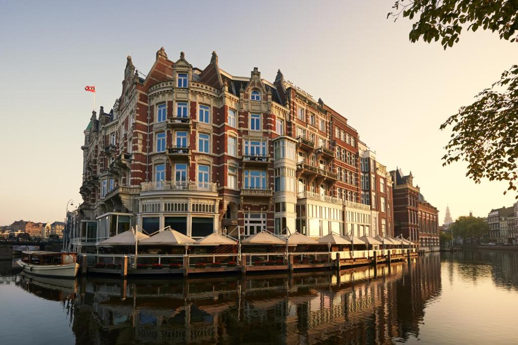 Prédio do De L’Europe Amsterdam, um dos hotéis de luxo, localizado na esquina, na costa do rio, sendo o prédio histórico, num tom vermelho, com várias janelas e torres
