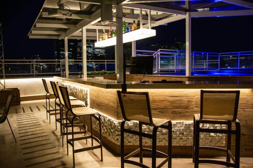 Bar perto da piscina a noite, iluminado e com cadeiras para o balcão. No terraço, com vista para a cidade. Foto para ilustrar post sobre hotéis perto do Consulado Americano no Rio de Janeiro.