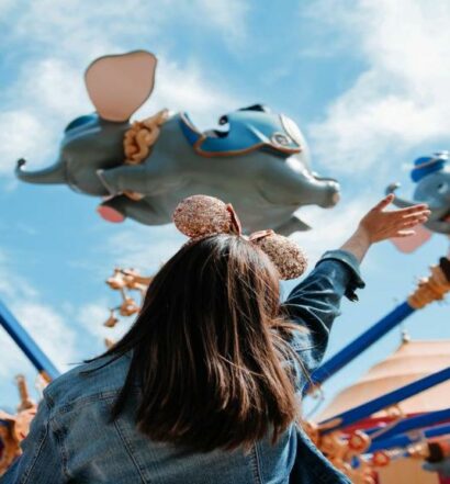criança de costas com tiara de orelhinhas do Mickey rosas acenando para um brinquedo com vários Dumbos que giram e parecem voar, para ilustrar o post de hotéis em Orlando para brasileiros
