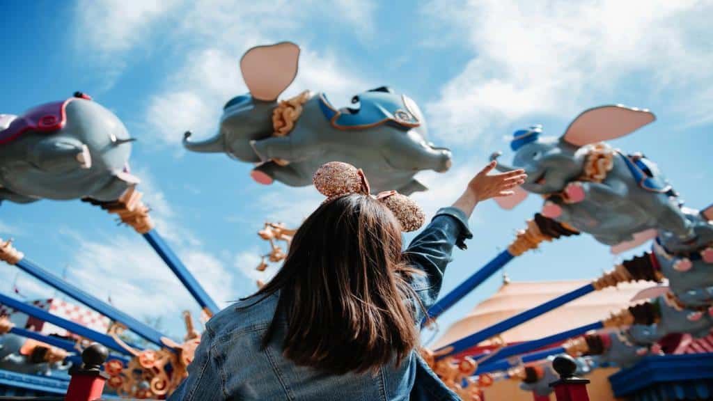 criança de costas com tiara de orelhinhas do Mickey rosas acenando para um brinquedo com vários Dumbos que giram e parecem voar, para ilustrar o post de hotéis em Orlando para brasileiros