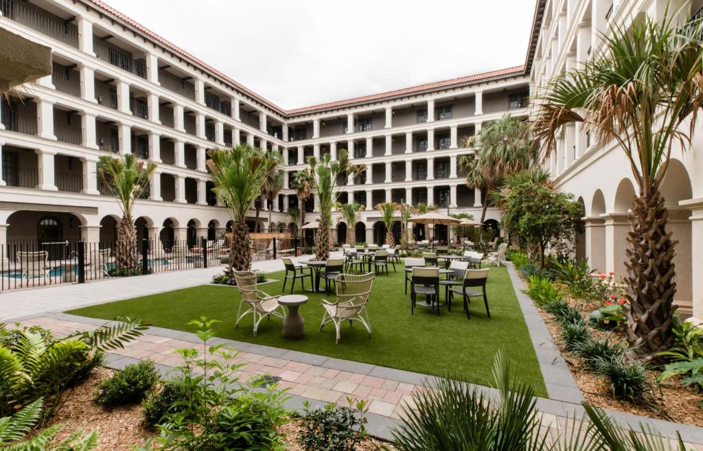 Jardim amplo do Estancia del Norte San Antonio, A Tapestry Hotel by Hilton  com muitas árvores, plantas, cadeiras e mesas para se sentar ao ar livre e, do lado esquerdo, há uma piscina