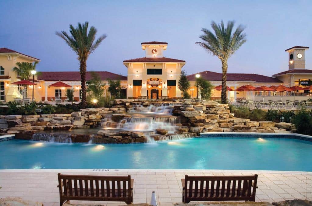 fachada iluminada ao entardecer com duas palmeiras e uma cascata com pedras que desagua em uma piscina no Holiday Inn Club Vacations At Orange Lake Resort, um dos resorts em Orlando