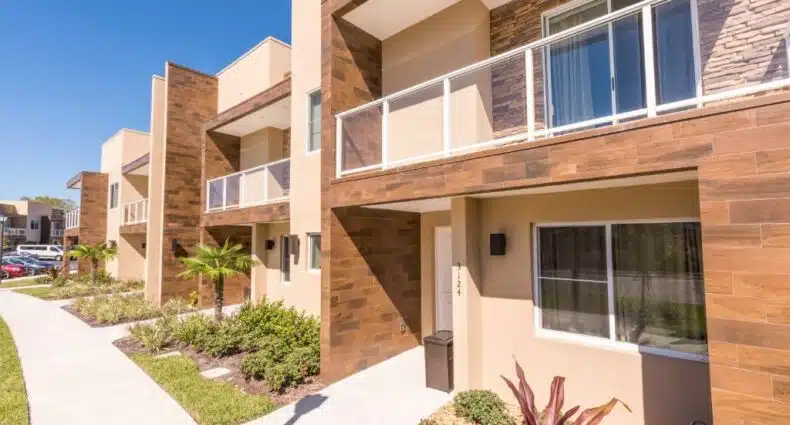 fachada do Magic Village Yards Trademark Collection, um dos hotéis com cozinha em Orlando, com dois andares modernos e tons rosados com gramado na frente