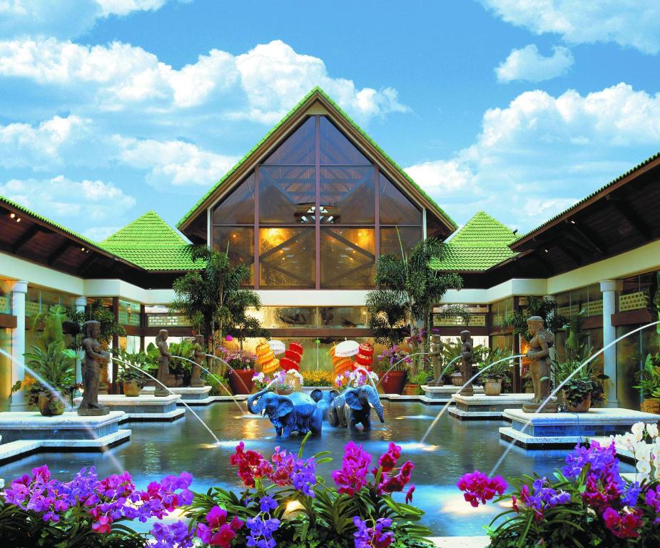 fachada de vidro em estilo de cabana com lago na frente com esculturas de elefantes e fontes dos lados, há flores roxas na frente no Universal's Loews Royal Pacific Resort, um dos hotéis da Universal em Orlando