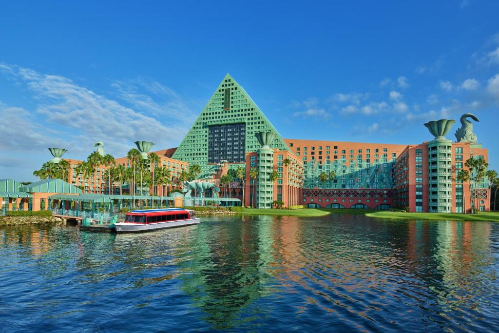 fachada em formato de triângulo com estátuas de cisnes acima com várias janelinhas e lago com barco que é transfer aquático para os parques no Walt Disney World Swan