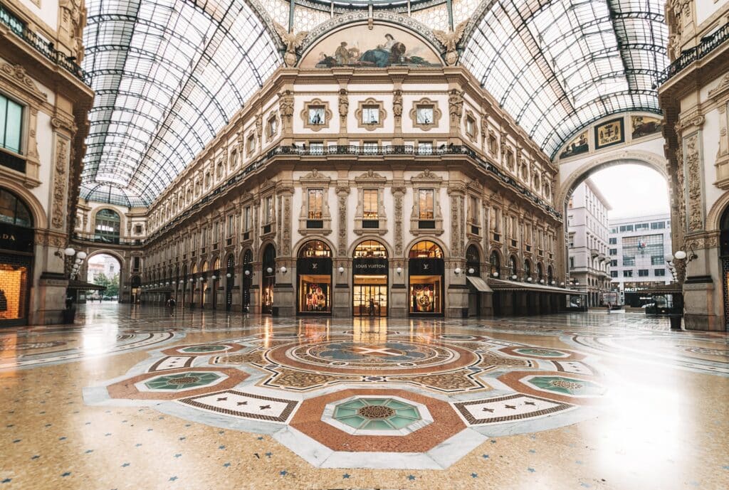 Parte interna da Galeria Vittorio Emanuele II em Milão, o teto é de vidro, a construção é em estilo renascentista, o chão é desenhado, assim como há algumas pinturas no topo das lojas