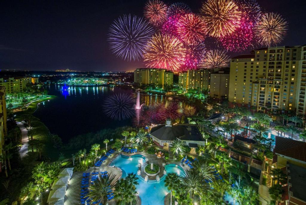 vista dos fogos coloridos à noite com a piscina abaixo com várias luzes e palmeiras ao redor da fachada do Wyndham Grand Orlando Resort Bonnet Creek um dos hotéis perto da Disney