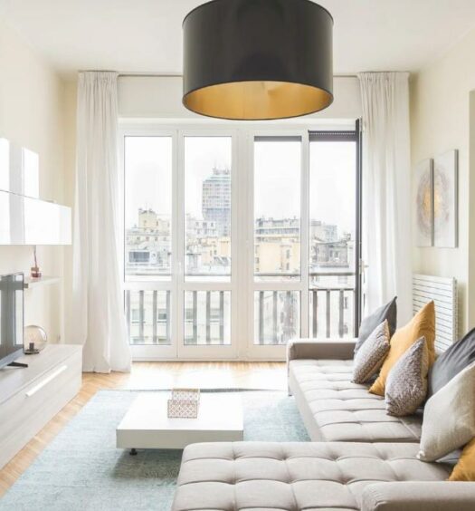 Sala de estar do Heart Milan Apartments San Sepolcro Duomo com uma ampla sacada, um sofá com diversas almofadas e um rack com televisão, para representar aluguel de temporada em Milão