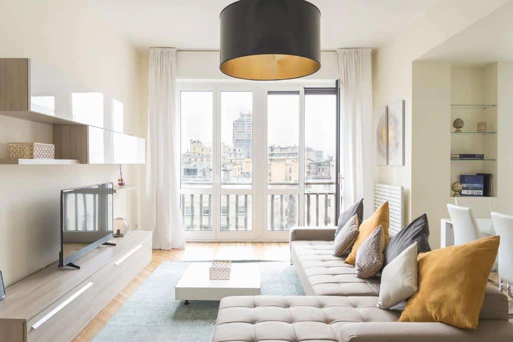 Sala de estar do Heart Milan Apartments San Sepolcro Duomo com uma sofá com diversas almofadas, uma varanda com cortinas, um rack com uma televisão e um lustre redondo preto, para representar airbnb em Milão