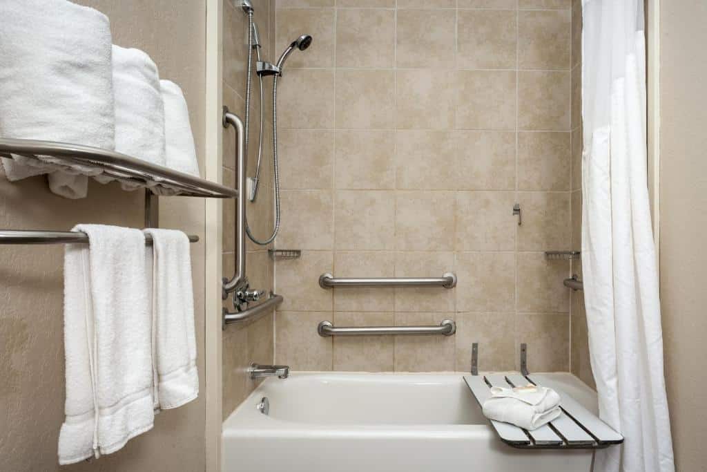 Banheiro adaptado do Holiday Inn San Antonio Northwest- SeaWorld Area, an IHG Hotel com barras de apoio, local para se sentar na banheira e diversas toalhas disponíveis em uma altura baixa