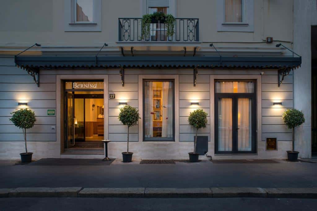 Fachada do Hotel Bernina com portas de vidro, alguns vasos com plantas entre as portas, há um toldo preto também