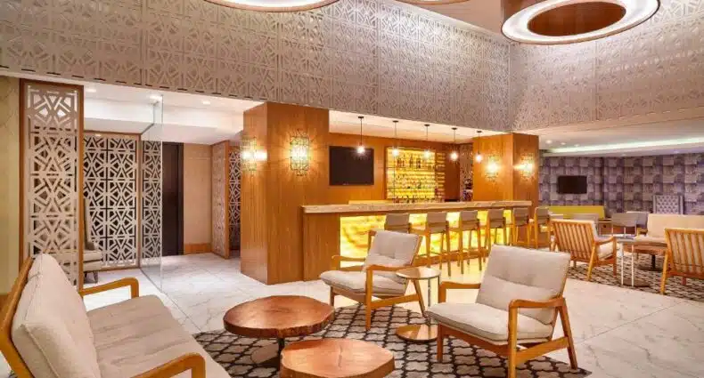 Visão da recepção do hotel, cadeiras na frente com uma mesa, atrás um balcão do bar. Luminárias redondas e grandes. Foto para ilustrar post sobre Hotéis perto do Consulado Americano em Porto Alegre.
