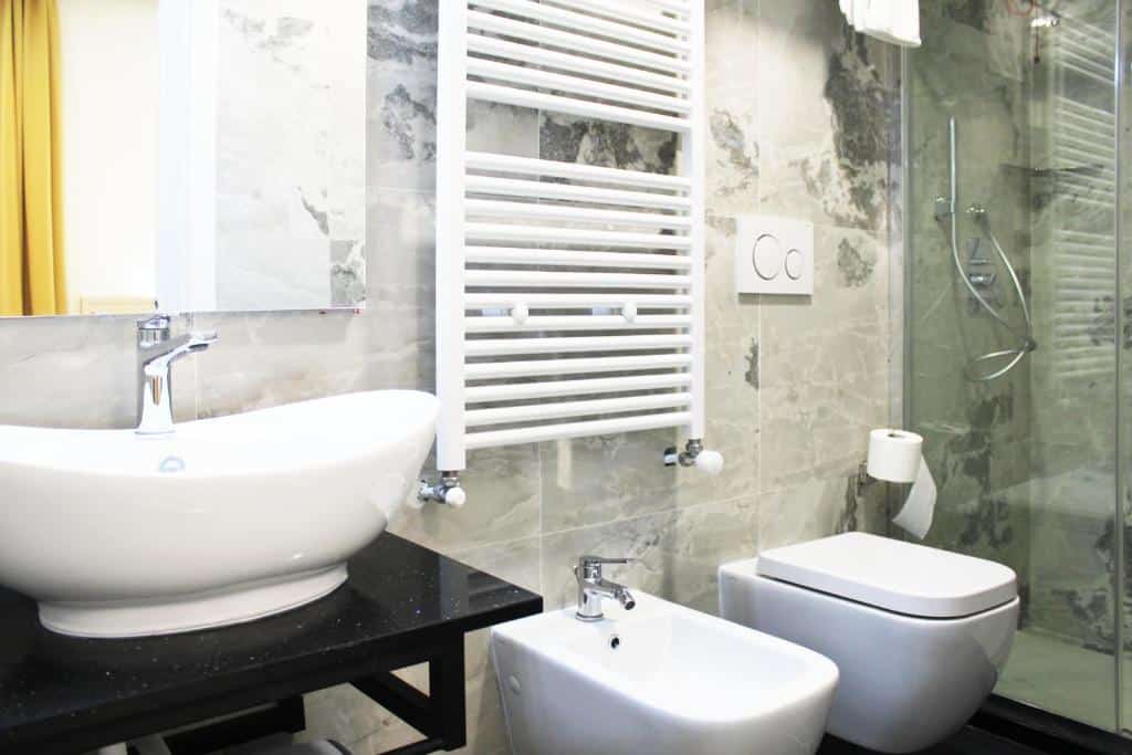 Banheiro do Hotel Metropoli com uma cuba branca em cima de uma mármore preto, um bidê, um vaso sanitário e um box
