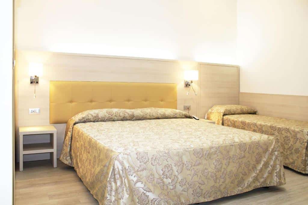 Quarto do Hotel Metropoli com uma cama de casal e uma de solteiro, há uma cabeceira com luminárias presas e o chão é de madeira, para representar hotéis baratos em Milão