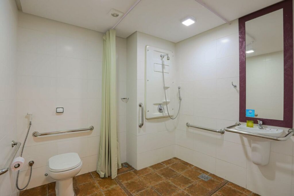 Banheiro com barras de apoio perto da privada, na parte do chuveiro e em volta da pia. Há também um espelho. Imagem para ilustrar post de hotéis em Belém do Pará.