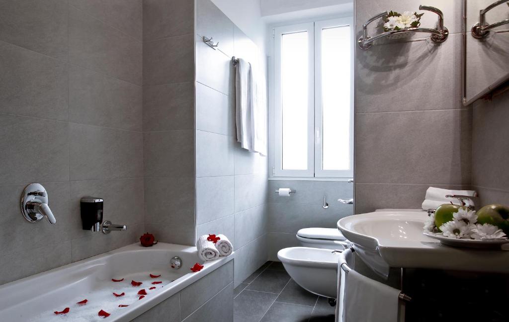 Banheiro do Hotel Ritter com uma pequena banheira, uma janela, um vaso sanitário, um bidê e uma pia com toalhas e flores