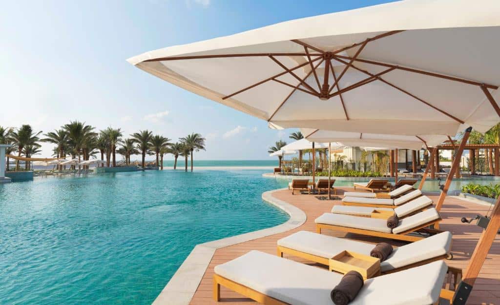 Piscina do InterContinental Ras Al Khaimah Resort and Spa, an IHG Hotel com borda infinita e vista para o mar, no deck, há espreguiçadeiras e guarda-sóis, com algumas árvores por perto