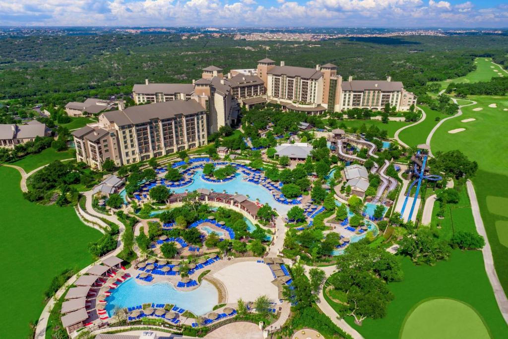 Vista aérea do JW Marriott San Antonio Hill Country Resort & Spa cercado por muito verde e árvores, dentro da propriedade há muitas piscinas com itens de parque aquático como tobogãs