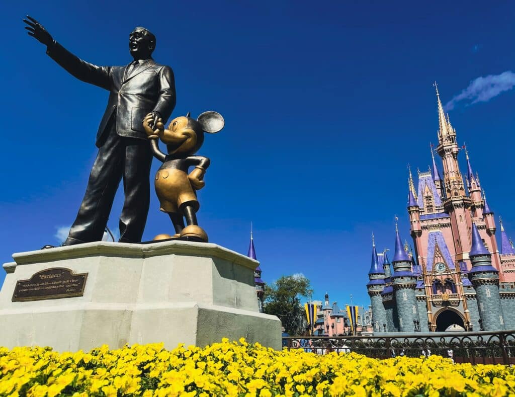 estátua do Walt Disney de mãos dadas com o Mickey com o castelo da Cinderela atrás no Parque do Magic Kingdom em Orlando