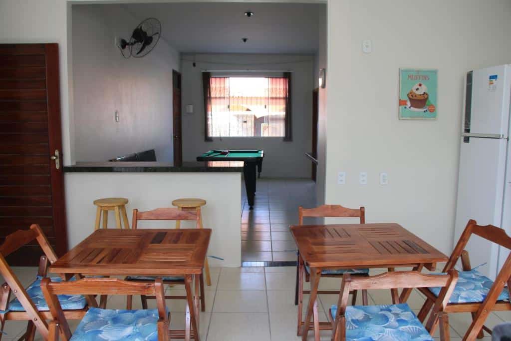 Cozinha e sala de jogos de um hostel em Parnaíba com mesas, cadeiras de madeira, geladeira e mesa de sinuca ao fundo.