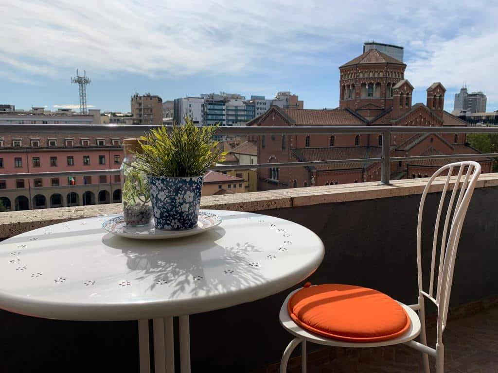 Uma pequena varanda no Milano 71 com uma mesinha redonda com um vaso de flor em cima e uma cadeira, para representar hotéis baratos em Milão