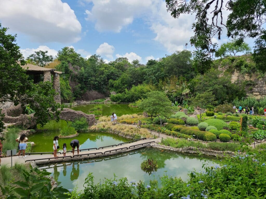 O Jardim Japonês de San Antonio com muito verde, lagos, uma pequena ponte, flores ornamentais e com algumas pessoas caminhando pelo local