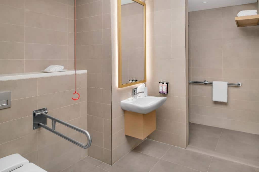 Banheiro adaptado do Mövenpick Resort Al Marjan Island com barras de apoio, cordão de emergência e pia e espelho mais baixos