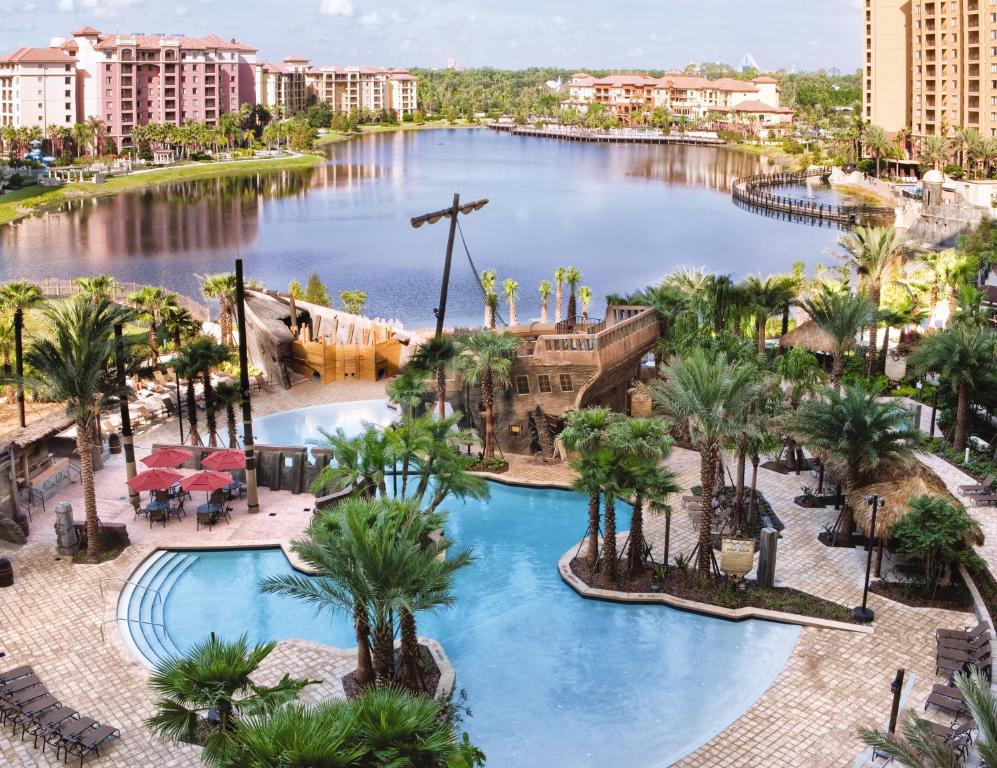 vista do lago e da piscina com tobogãs e um barco pirata como brinquedo aquático, há algumas palmeiras e cadeiras de praia no Club Wyndham Bonnet Creek, uma das opções aos hotéis perto da Disney