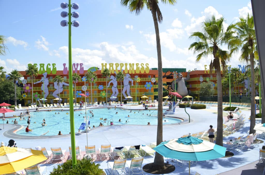 piscina em forma de lagoa com algumas palmeiras e a fachada atrás para os quartos com silhuetas de pessoas dançando e um Mogli e Balu enormes ao lado no Disney's Pop Century Resort