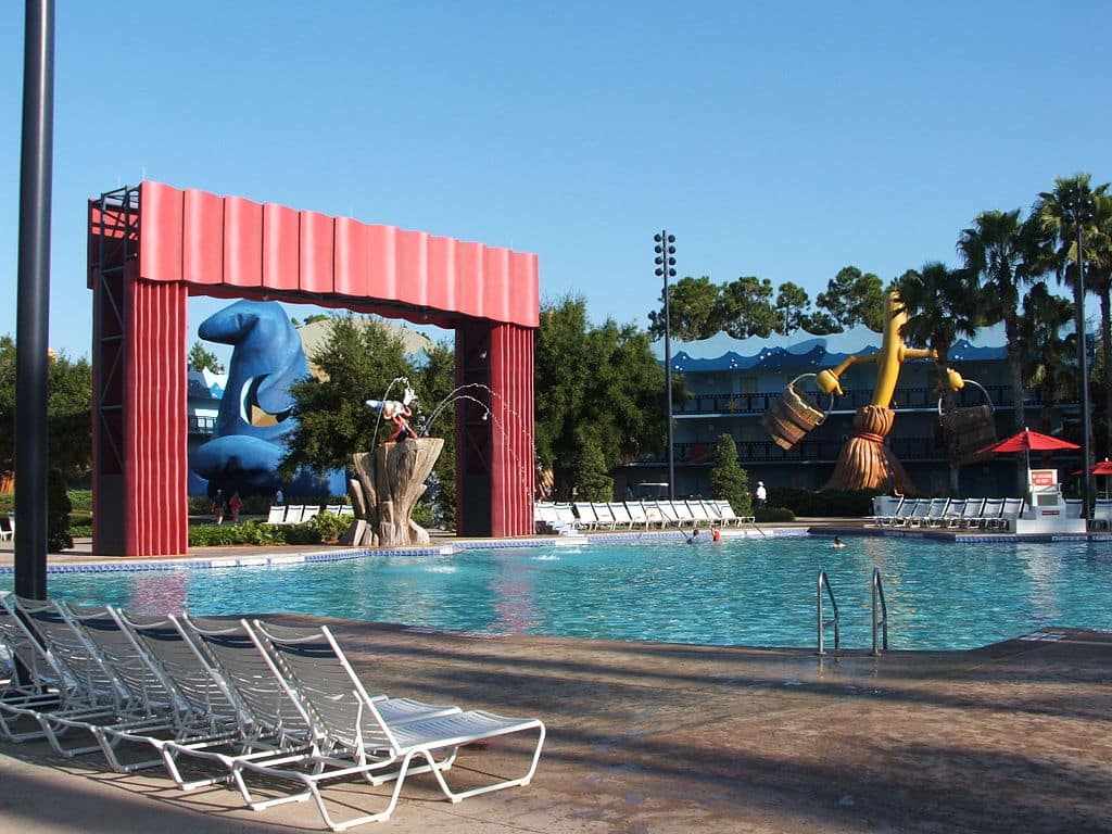 piscina do Disney's All-Star Movies Resort com decoração inspirada no filme Magia, com o Mickey de mago, o chapéu do filme gigante atrás e as vassouras mágicas com bracinhos também enormes na fachada