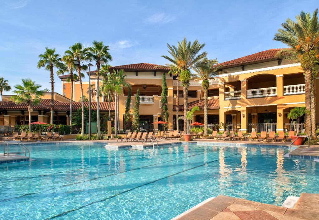 piscina com algumas palmeiras e cadeiras de praia ao redor, a fachada está atrás do Floridays Orlando Two & Three Bed Rooms Condo Resort, um dos hotéis da Disney em Orlando