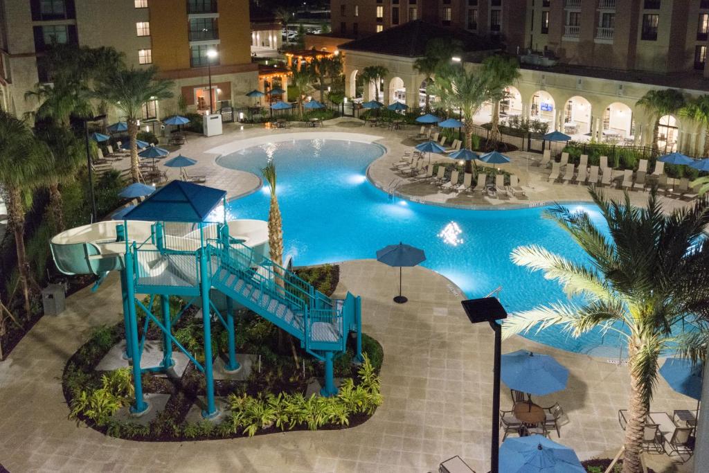 piscina à noite com bordas sinuosas e cadeiras de praia ao redor, com um tobogã alto acessado por uma escadinha no Homewood Suites By Hilton Orlando Flamingo Crossings, Fl, um dos hotéis perto da Disney