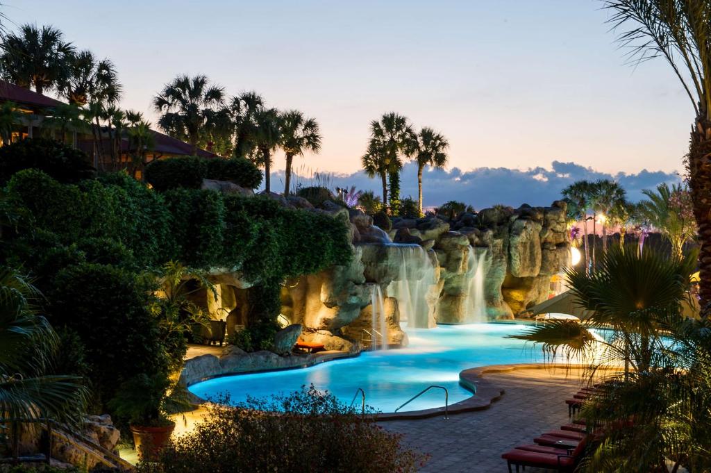 piscina em forma de lagoa com várias cascatas que caem ali, com cadeiras e palmeiras ao redor, criando um ambiente meio mágico com cadeiras no Hyatt Regency Grand Cypress Resort, um dos hotéis para brasileiros em Orlando