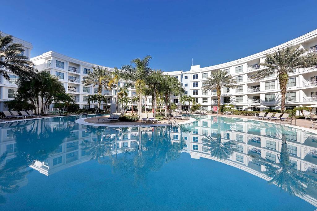 fachada grande que rodeia uma piscina que tem uma ilha no meio, com palmeiras e cadeiras de praia, no Meliá Orlando Celebration, um dos hotéis da Disney em Orlando